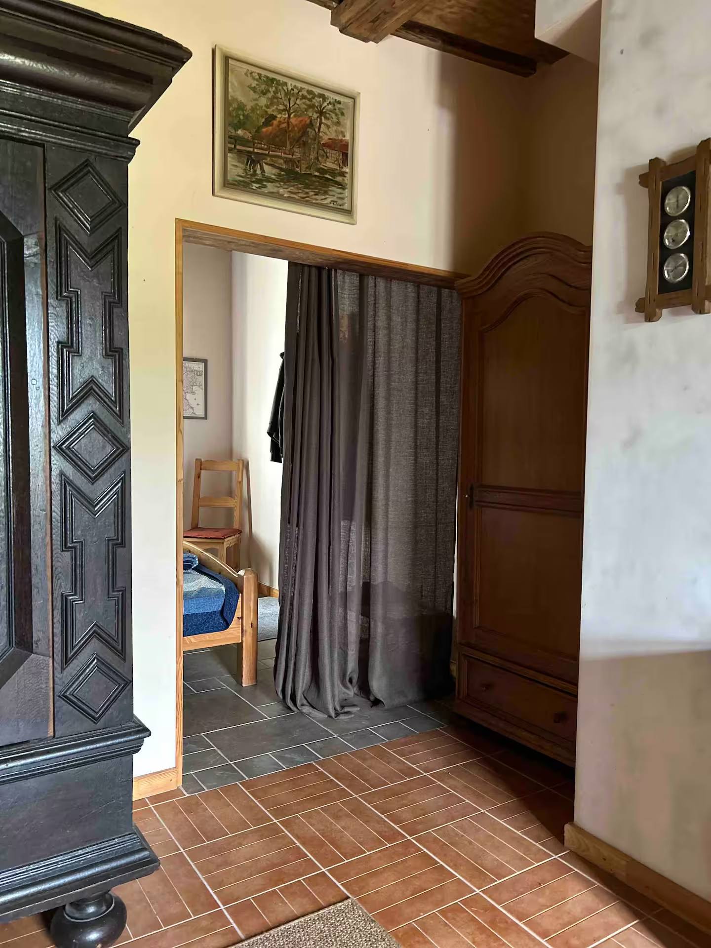 Blick durch eine Tür in einen weiteren Raum, im Vordergrund ein hoher antiker Holzschrank mit Schnitzwerk, der Boden hat Terrakottafliesen.
