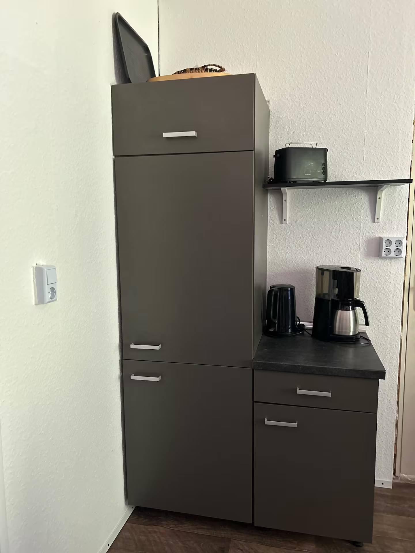 Hoher Kühl- und Gefrierschrank neben einem Unterschrank mit Kaffeemaschine und Wasserkocher, darüber ein Regalbrett mit Toaster.